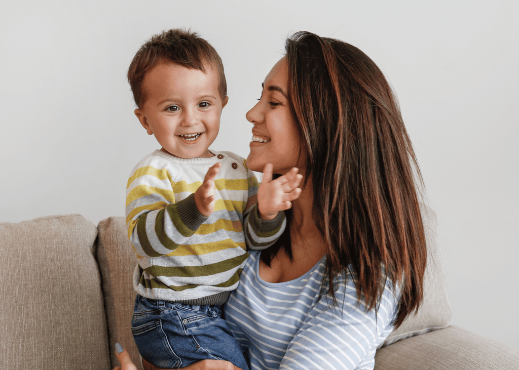 A happy mother smiling at her child who is clapping in joy