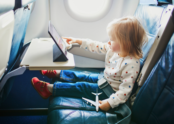 Female toddler sitting on plane doing activities on ipad