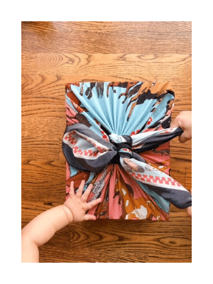 gift wrapped in fabric, baby hand and toddler's hand on wooden floor