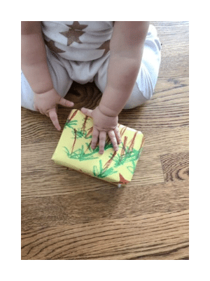 gift wrapped in kid's drawing, baby hands on wooden floor.