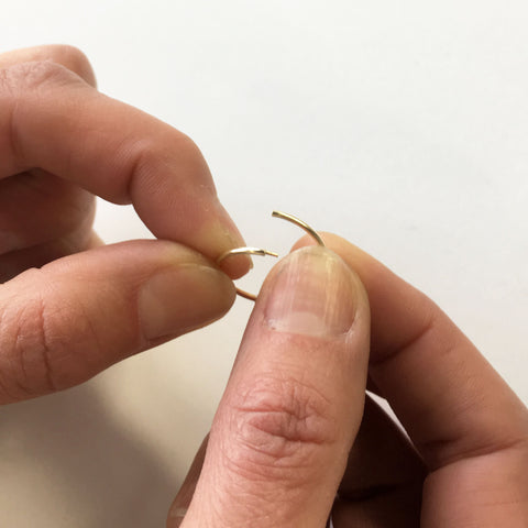 A golden hoop earring opened to show how to put it on 