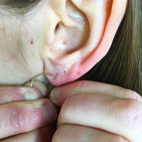 A lady putting on a gold hoop earring to her ear 