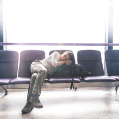 A woman sleeping on airport chairs with her head resting on her backpack