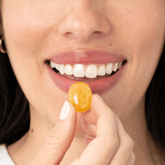 A close-up of a woman smiling as she places a Kindroot Defend reishi + vitamin C  lozenge in her mouth.