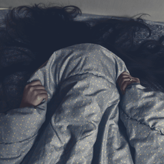 A woman lying in bed and pulling the blanket over their face as though having a nightmare
