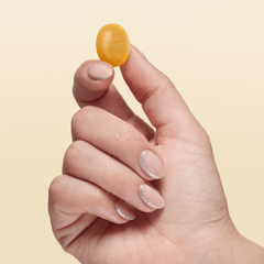 A hand holding an orange Kindroot Snooze lozenge between thumb and index finger on a light yellow background