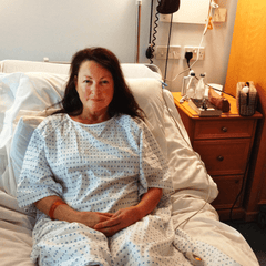 A middle-aged woman with brown hair in a hospital gown sitting in a hospital bed before surgery