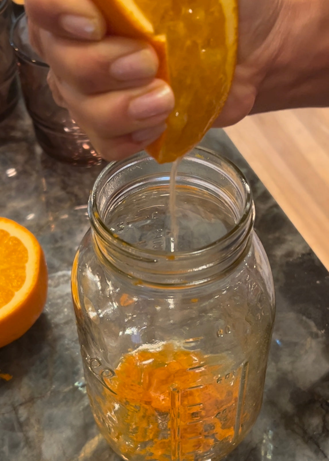 Squeezing juice from orange into mason jar with orange zest