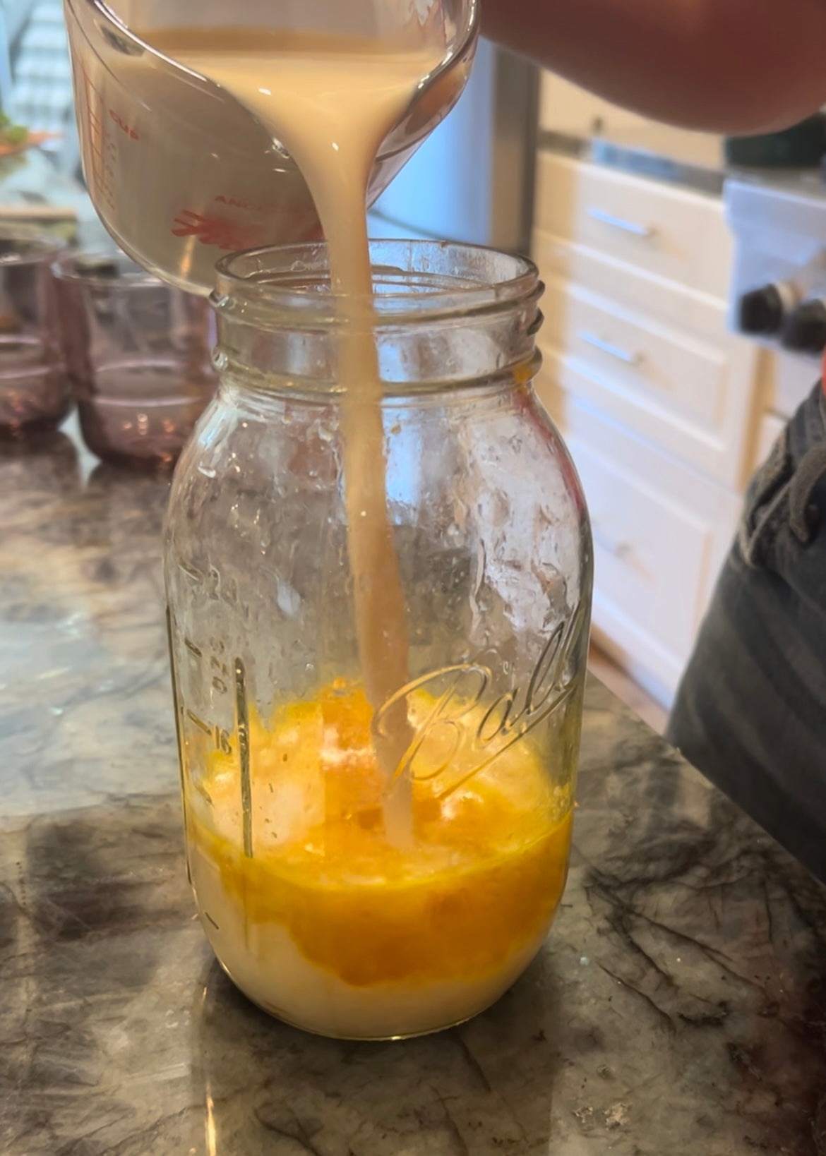 Pouring evaporated milk into glass with orange juice and orange zest