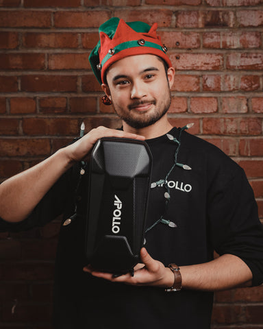 a man in a chrstmass elf hat is holding an apollo bag