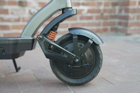 side view of the front wheel of the Apollo City 2022 e-scooter that is standing upright in front of a brick wall