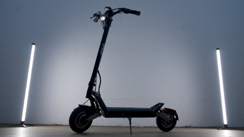 left-side view of the Apollo Phantom e-scooter standing in front of a white wall with two vertical neon lights on each side. 