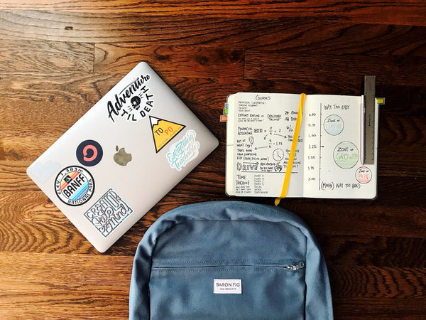 overhead view of a wooden table with a backpack, laptop, and journal