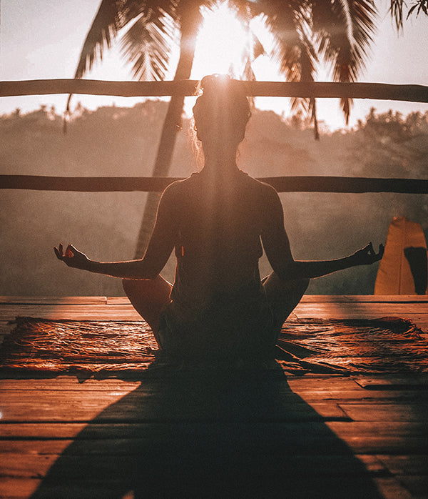 A picture of a woman meditating outdoors during sunset
