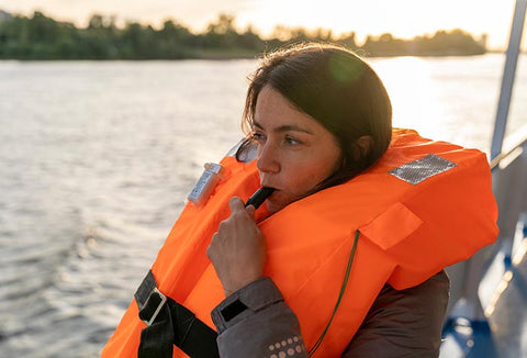 A woman wearing a life vest on a boat, blowing a rescue whistle.