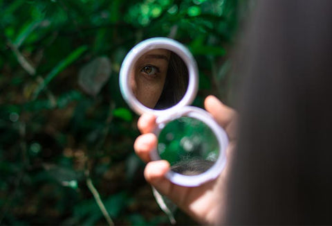 A woman holding a handheld mirror to use for signaling in the woods.