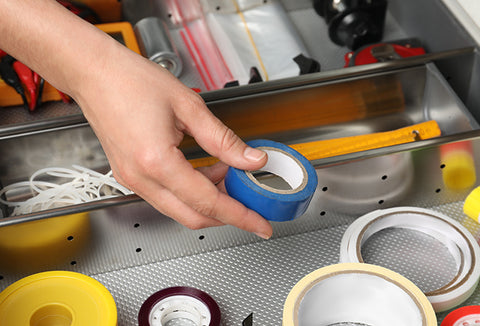 A hand holding a small roll of painter's tape from a drawer full of other types of tape.