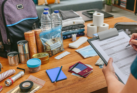 A person using a pen to check off a packing checklist on a clipboard. In front of them is a table full of supplies.