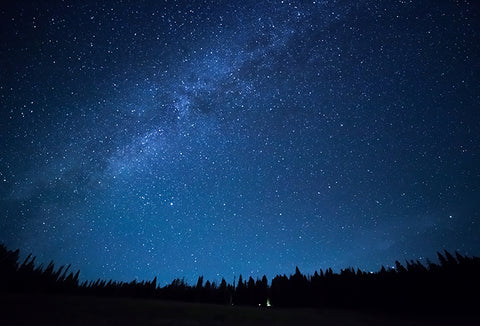 A wide night sky in various shades of dark blue, with stars and clouds scattered around.