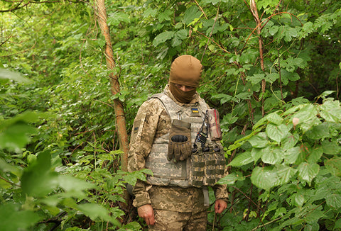 A man dressed in light brown and light green camouflage hidden in a green forest.