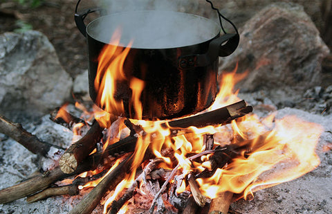 A black pot of water hanging over a roaring fire built on top of stones.