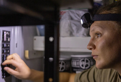 Woman wearing a headlamp while fixing a breaker.