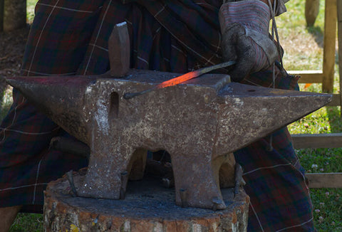 Someone wearing heat-protectant gloves working with hot metal on an anvil.