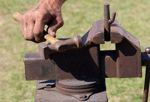 A person using a hammer to create and work on blacksmithing tools.