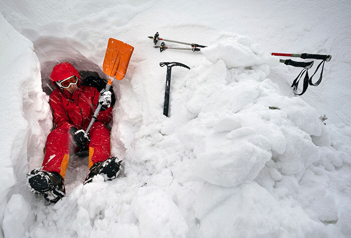 man digging a shelter in the snow with a shovel