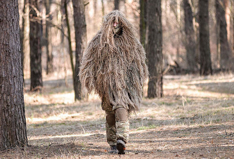 A man wearing a beige, desert-toned ghillie suit.