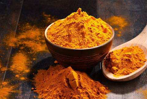 Turmeric powder in a bowl and spoon scattered across a table.