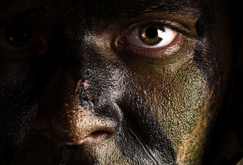 A zoomed-in view of a person's face, painted in shades of dark green for camouflage.