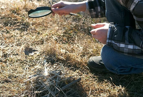 Person lighting a fire using a magnifying glass.