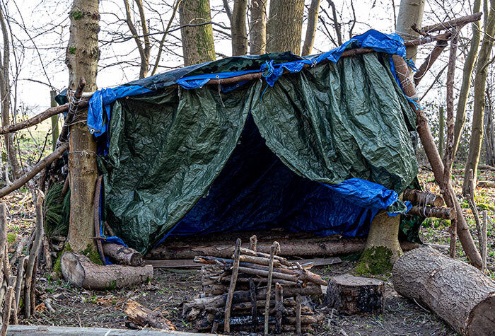 A shelter in the woods built from branches and tarps.