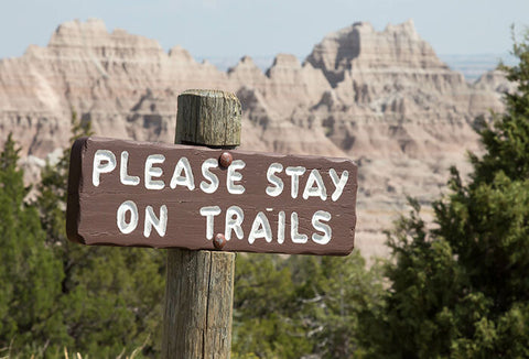 A hiking sign telling people to stay on the trail.