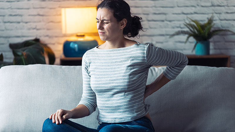 Woman showing signs of a sore lower back. cbd yoga. yoga and cbd. is cbd oil and yoga good for you? why cbd with yoga is the best idea ever.