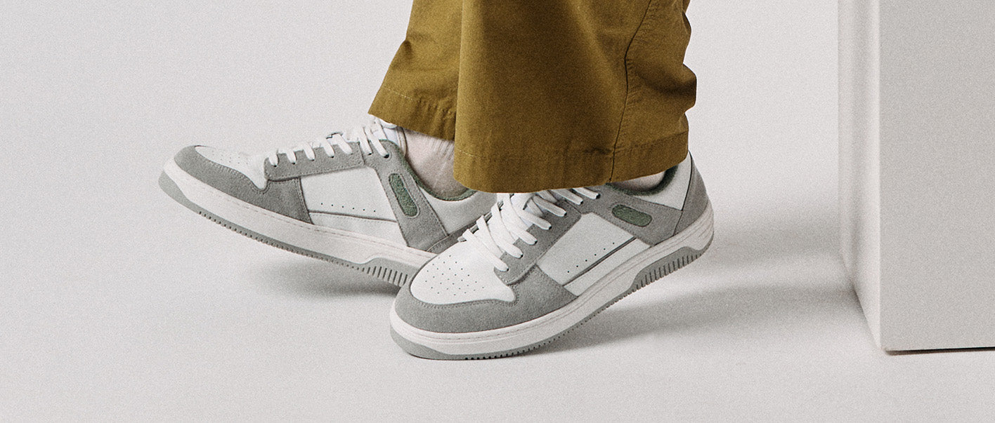 Les pieds d'une personne portent des chaussures basses blanches sneakers et un pantalon marron. Le site sneakers semble être fait sur mesure.