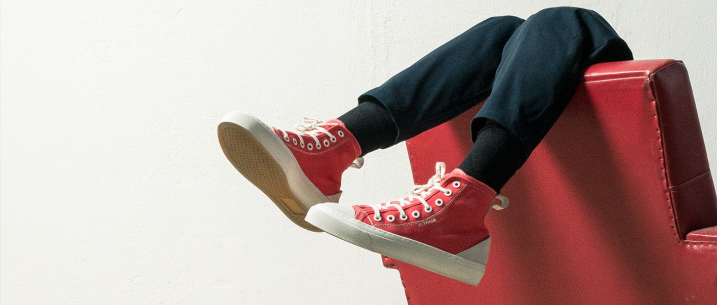A person sitting on a red chair with their feet up, wearing high top sneakers and custom women shoes.
