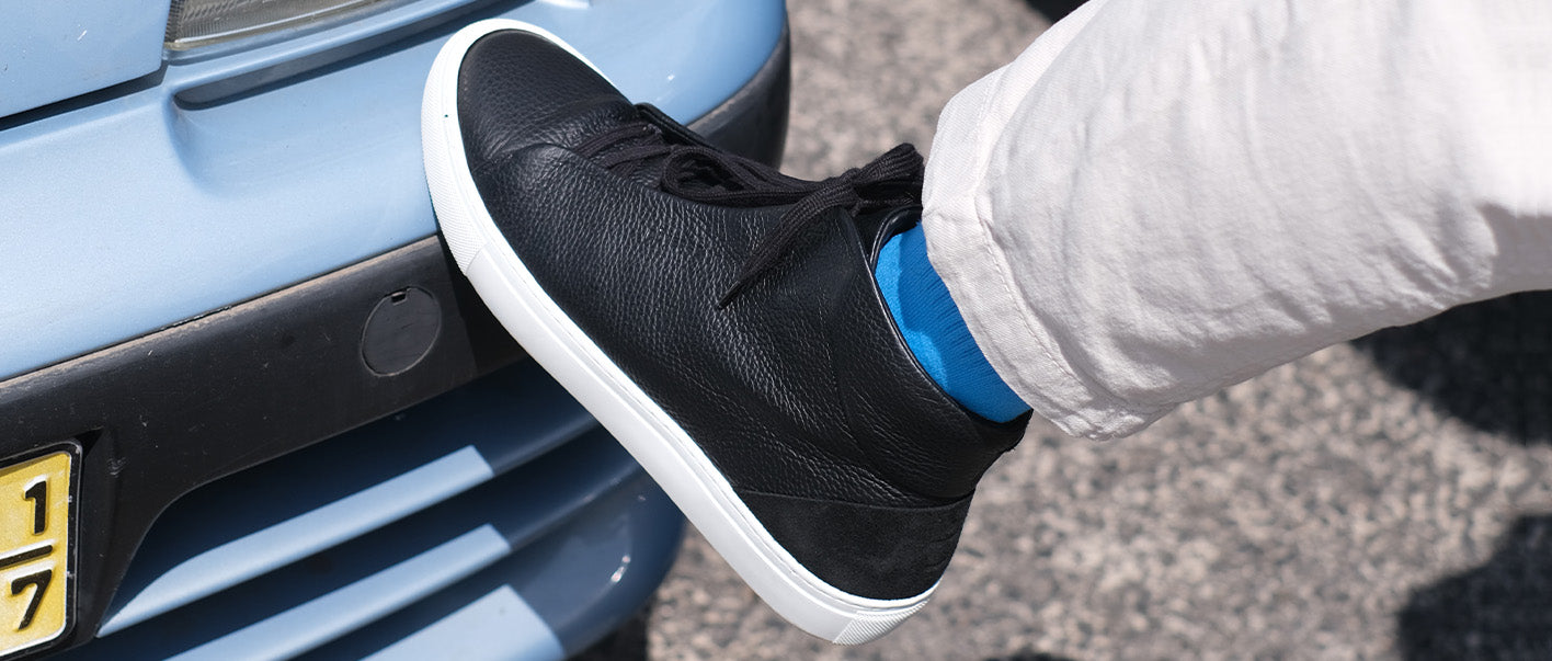 A person's foot in custom shoes resting on a car bumper.