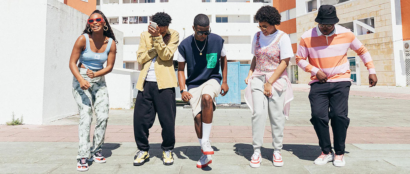 Four young people wearing custom shoes stand on a sidewalk.
