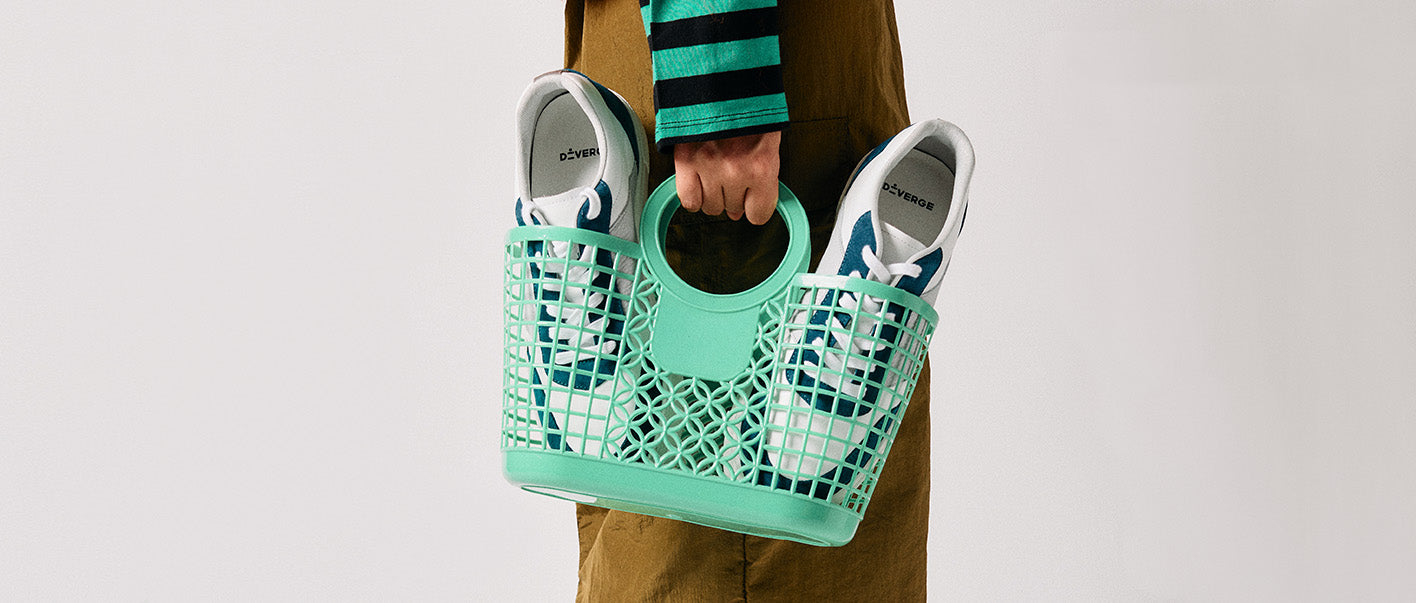 Eine Person hält eine grüne Netztasche mit neuen sneakers und maßgefertigten Schuhen.