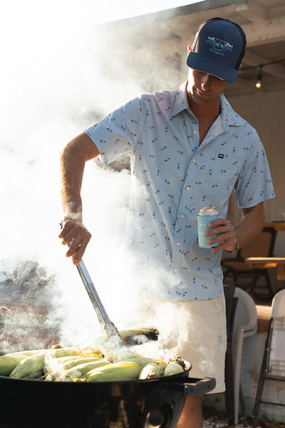 man cooking corn on grill outside with drink in hand