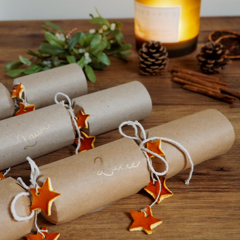 three paper crackers with orange stars on them next to a candle.