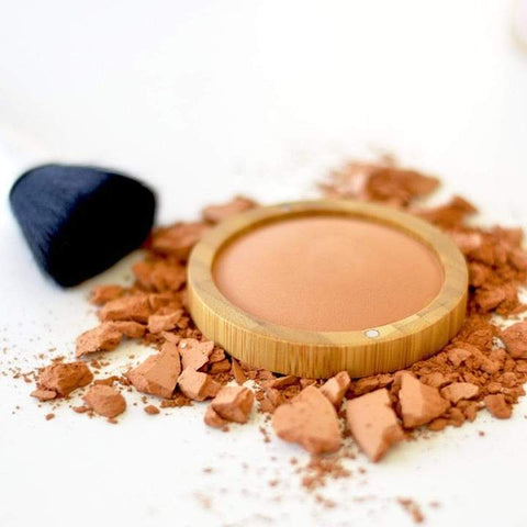 crushed and pressed natural glow powder with a make up brush laying next to it.