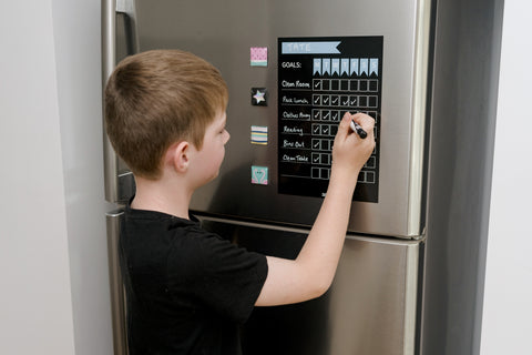 Boy writing on blue magnetic goal chore chart on fridge