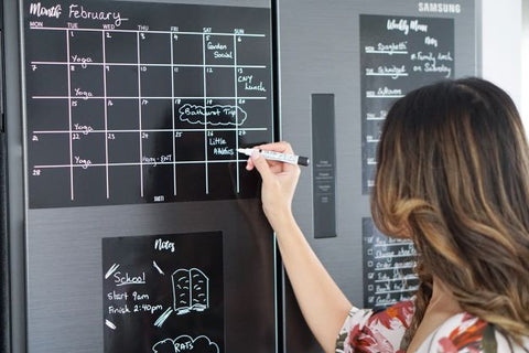 Lady writing on her black magnetic fridge planner calendar