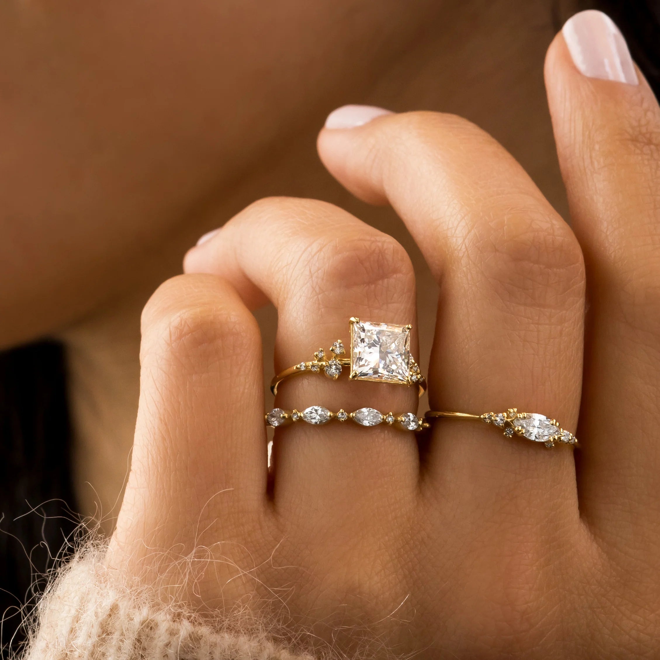 A bold 1ct princess cut diamond ring set in yellow gold with a pavé band, worn on the finger, capturing the clean lines and intense sparkle of the stone against a soft pink background.