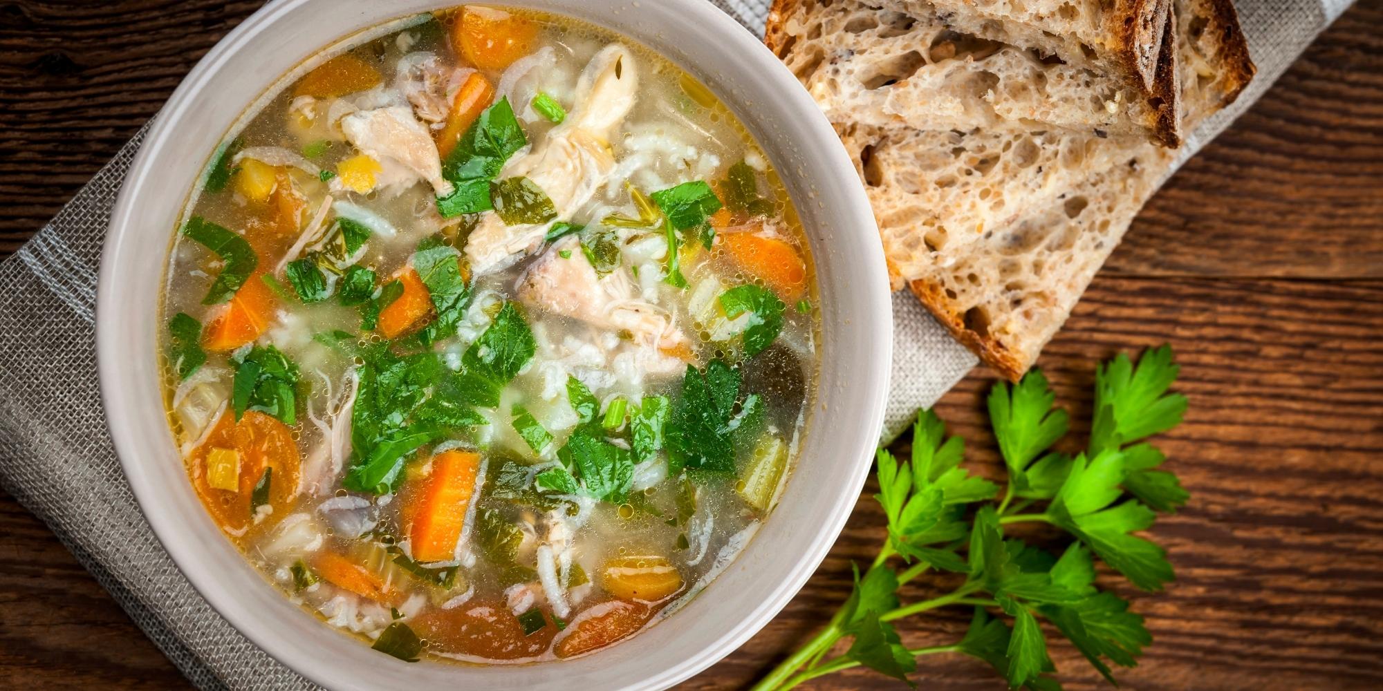 Chicken rice soup with vegetables in bowl and bread from above.