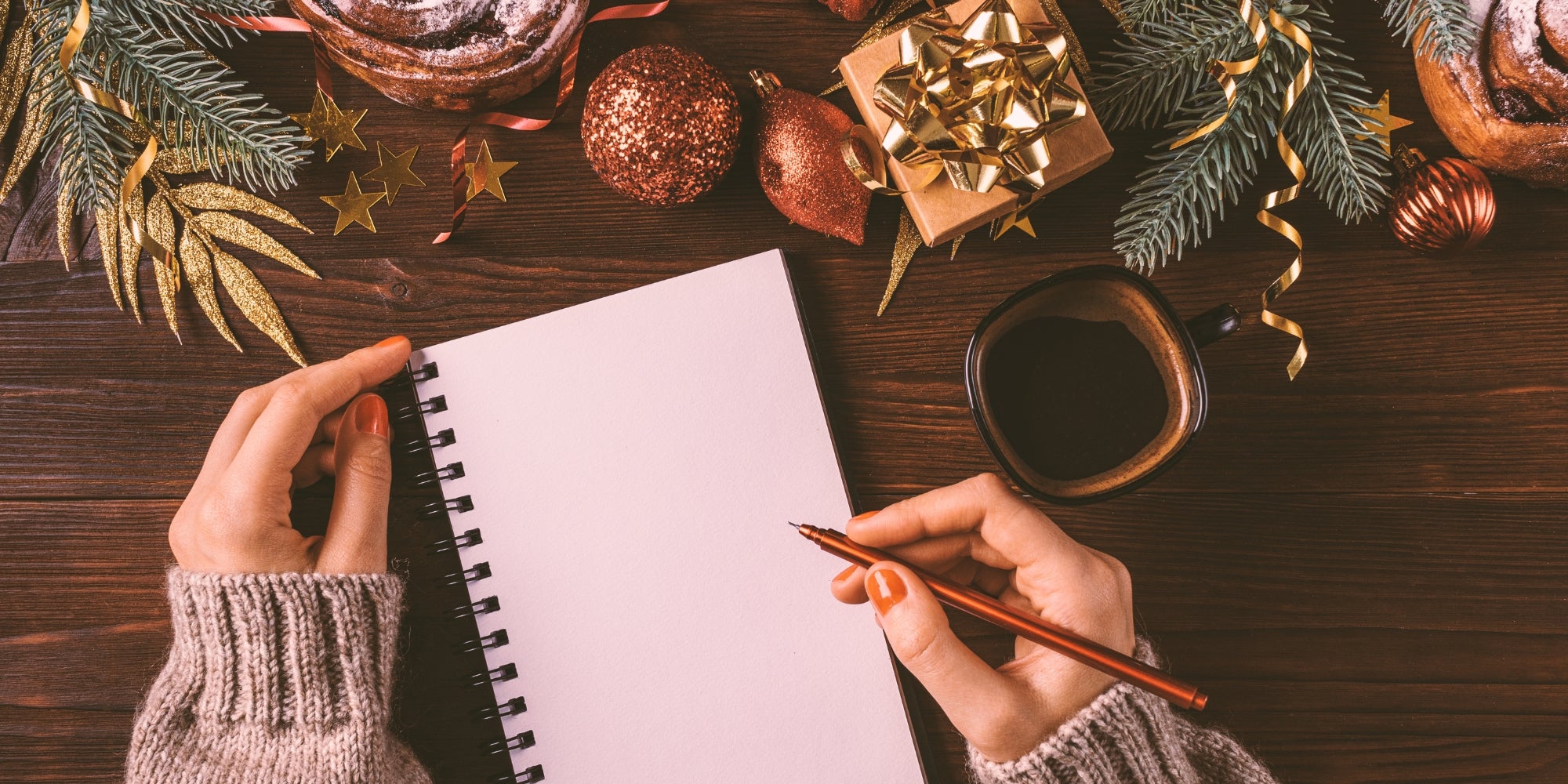 Females hands write in blank notebook next to cup of coffee. 