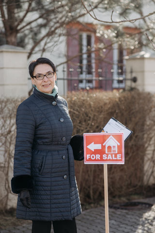 woman in black jacket holding red and white for sale sign